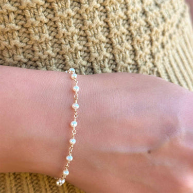 A gold-colored bracelet with small gold links and freshwater pearls, featuring a lobster clasp.