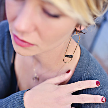 Close-up of a woman wearing gold safety pin earrings and rings with a blurred background #stone-black_spinel