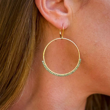 Gold hoop earring with green beads worn by a person